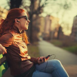 Red-haired woman listening to music on bench